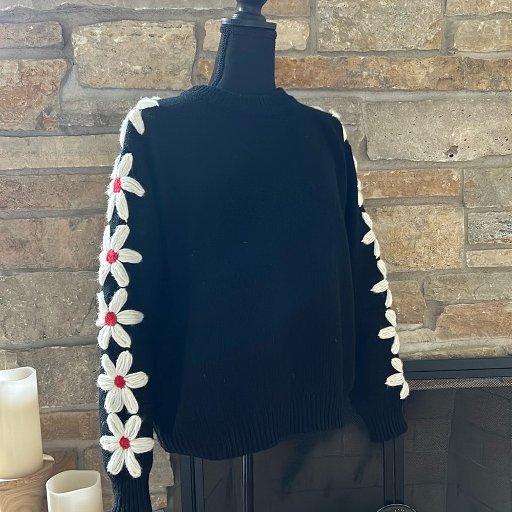 Black sweater with floral detailing on the sleeves.